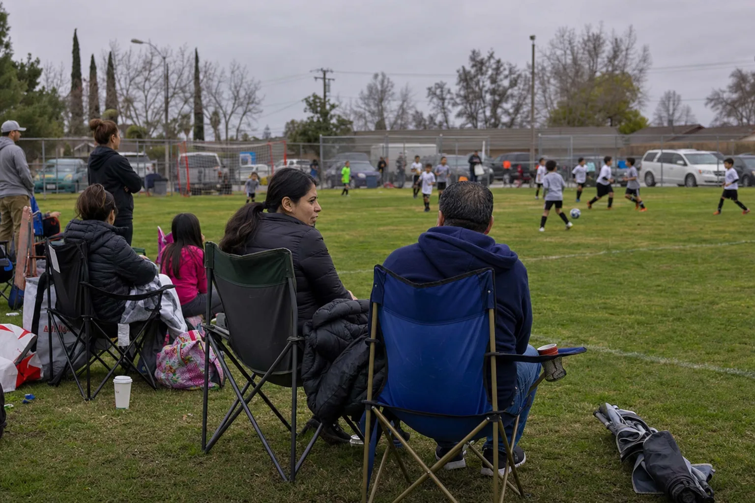 Parents watching a youth soccer game from folding chairs on the sideline